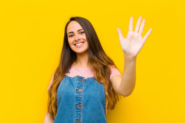 Jovens bonitas mulher sorrindo e olhando amigável, mostrando o número cinco ou quinto com a mão para a frente, contando para baixo