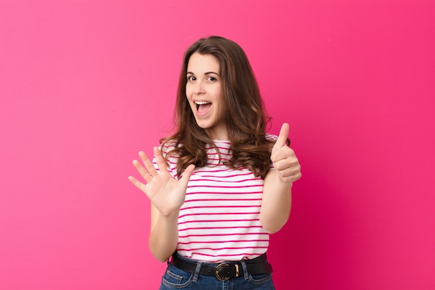 Jovens bonitas mulher sorrindo e olhando amigável, mostrando o número seis ou sexto com a mão para a frente, contando com a parede rosa