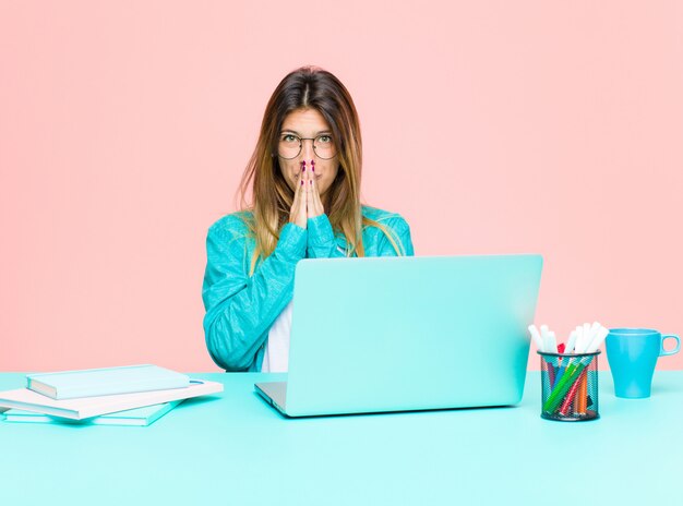 Jovens bonitas mulher trabalhando com um laptop feliz e animado, surpreso e espantado cobrindo a boca com as mãos, rindo com uma expressão fofa