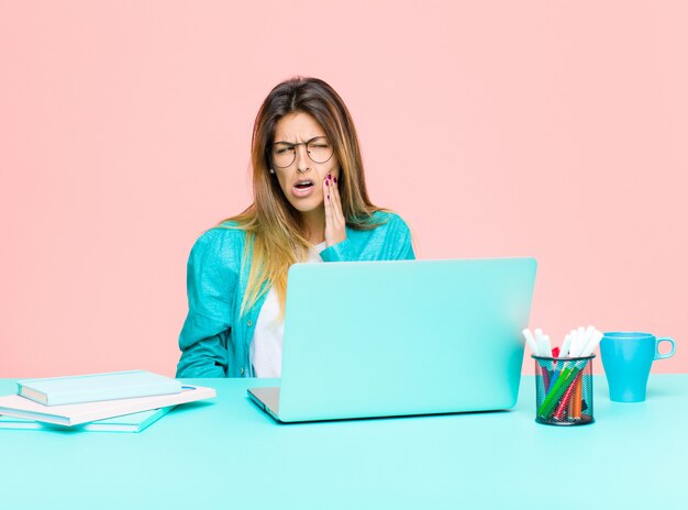 Jovens bonitas mulher trabalhando com um laptop segurando a bochecha e sofrendo dor de dente dolorosa, sentindo-se doente, infeliz e infeliz, procurando um dentista