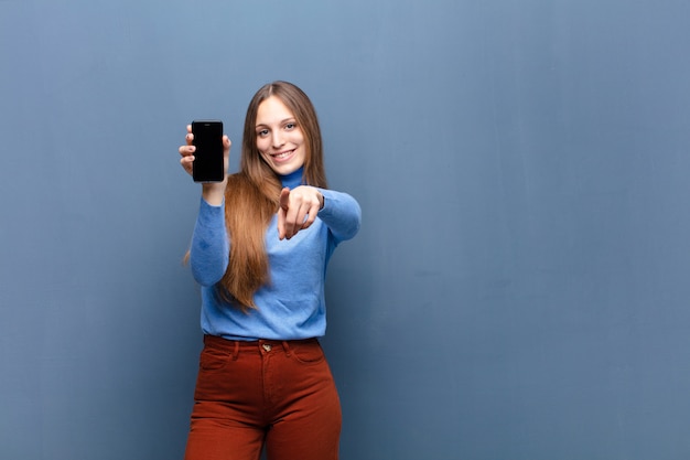 Foto jovens bonitas mulher usando um telefone inteligente contra a parede azul com um copyspace