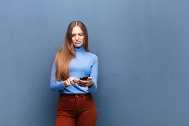 Jovens bonitas mulher usando um telefone inteligente na parede azul com um espaço de cópia