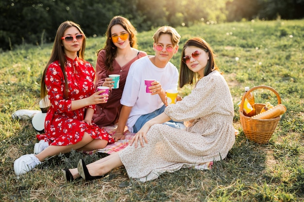 Foto jovens bonitos em um piquenique de verão em óculos de sol com bebidas