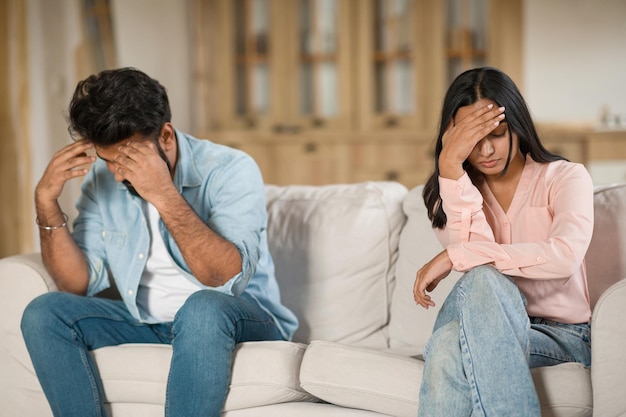 Jovens casados hindus angustiados sentados separados em casa no sofá