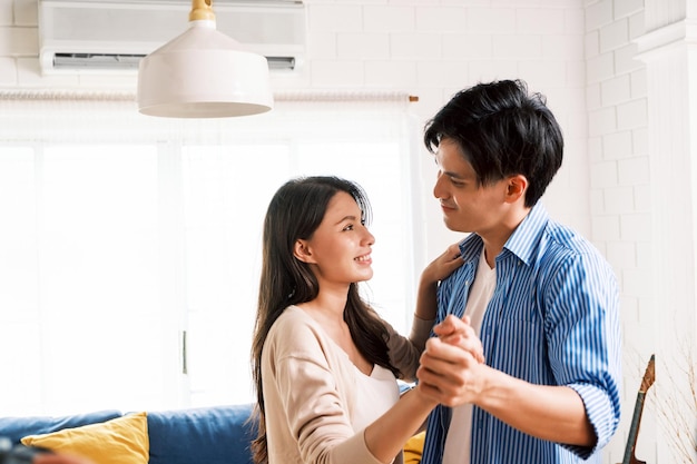 Jovens casais asiáticos atraentes gostam de ter uma linda dança romântica na sala de estar do apartamento Uma família passa bons momentos juntos depois de se mudar para uma nova casa Imagem com espaço de cópia