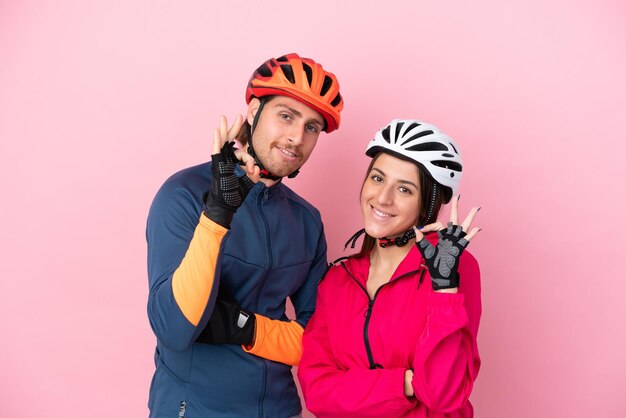 Jovens ciclistas caucasianos isolados em fundo rosa, mostrando um sinal de ok com os dedos