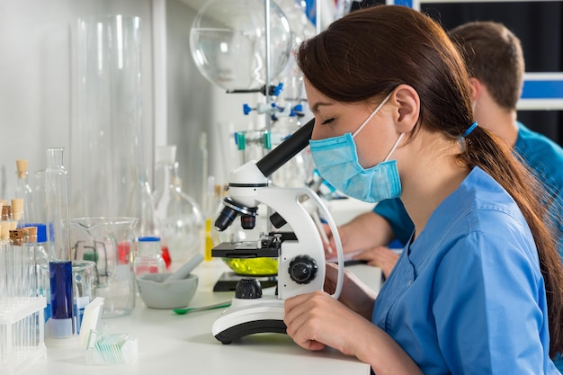 Jovens cientistas e cientistas de uniforme estão olhando através de um microscópio e fazendo algumas pesquisas em um laboratório. Conceito de saúde e biotecnologia