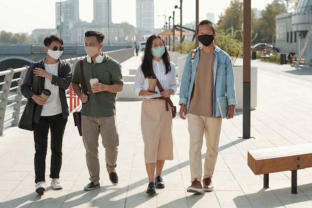 Jovens colegas com máscaras protetoras dando um passeio no parque em um dia ensolarado