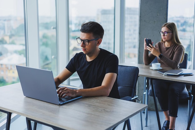 Jovens colegas no escritório na área de trabalho com um laptop Jovens colegas modernos em roupas casuais inteligentes trabalham enquanto trabalham no escritório