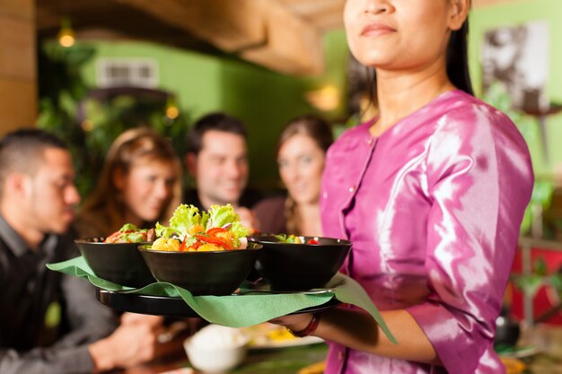 Jovens com garçonete comendo no restaurante tailandês