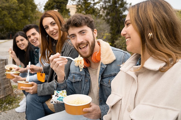 Jovens com máscara facial no pulso se divertindo comendo comida para viagem no parque