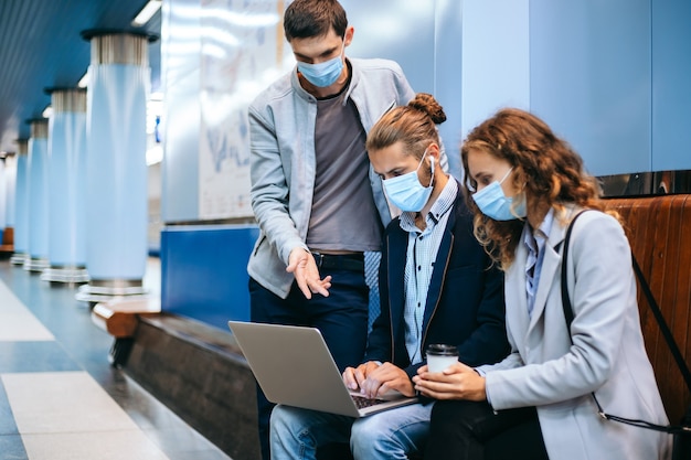 jovens com máscaras protetoras usando um laptop na plataforma do metrô