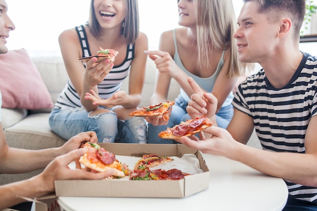 Jovens comendo pizza. Grupo de amigos almoçando dentro de casa. Amigos engraçados juntos.