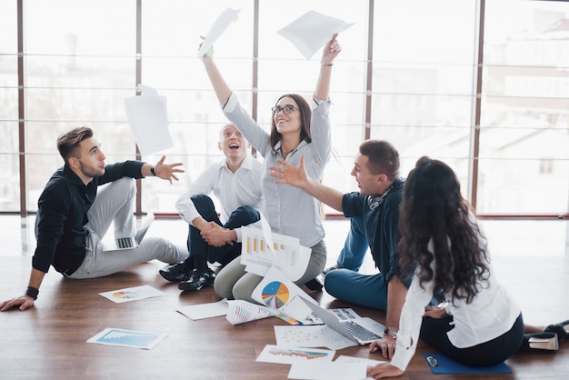 Jovens criativos no escritório moderno. grupo de jovens empresários estão trabalhando em conjunto com o laptop. freelancers sentados no chão. realização corporativa de cooperação. conceito trabalho em equipe