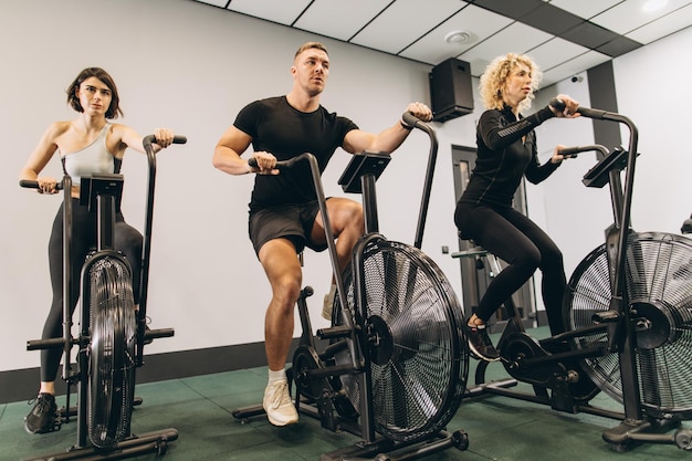 Jovens e mulheres usando bicicleta de ar para exercícios aeróbicos no ginásio de treinamento cruzado