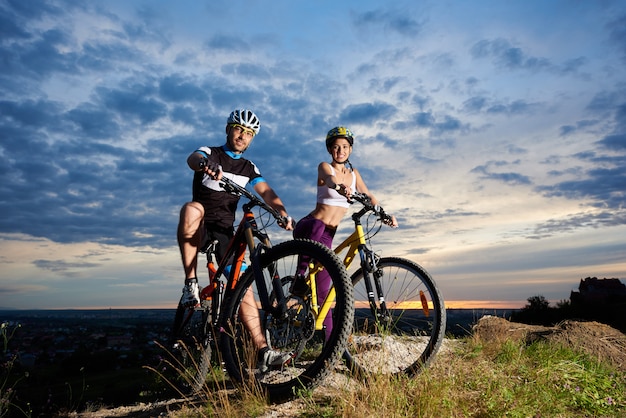 Jovens em bicicletas de montanha no topo de uma colina sob um céu mágico ao pôr do sol.