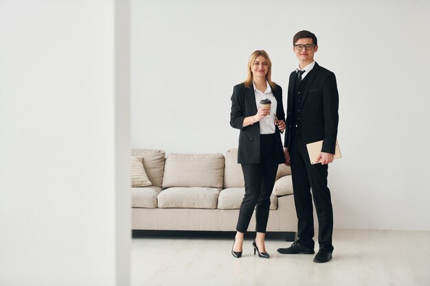 Jovens em pé com mulher dentro de casa perto do sofá contra a parede branca