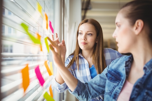 Jovens empresárias discutindo sobre notas adesivas na janela