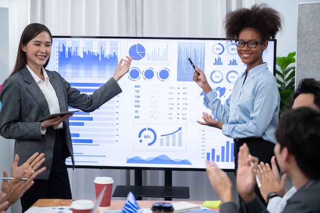 Jovens empresários africanos e asiáticos apresentam o painel de análise de dados juntos no ecrã de televisão numa reunião moderna Apresentação de negócios com um grupo de empresários na sala de conferências Concord