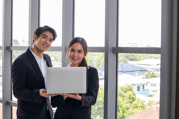 Jovens empresários asiáticos e mulheres de negócios consultam o trabalho juntos. Observando o notebook no local de trabalho