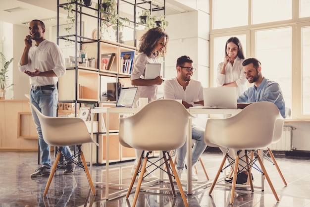 Jovens empresários bem sucedidos estão usando gadgets compartilhando ideias e sorrindo enquanto trabalham no escritório