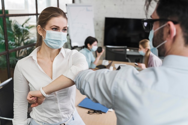 Foto jovens empresários com máscaras médicas durante reunião fazendo saudação de cotovelo