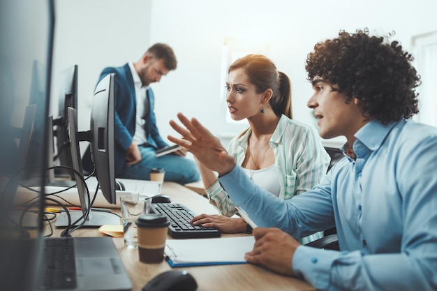 Jovens empresários discutindo algum documento enquanto trabalhava no computador desktop no escritório casual.