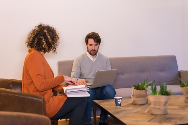 Jovens empresários em uma reunião de negócios em sofás com um computador e um bloco de notas