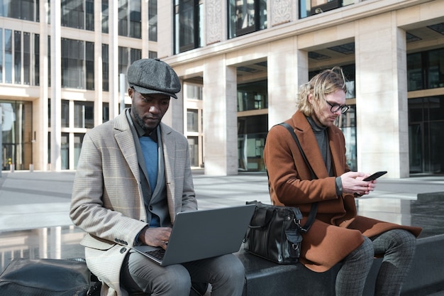 Jovens empresários usando laptop e celular no trabalho enquanto estão sentados na cidade