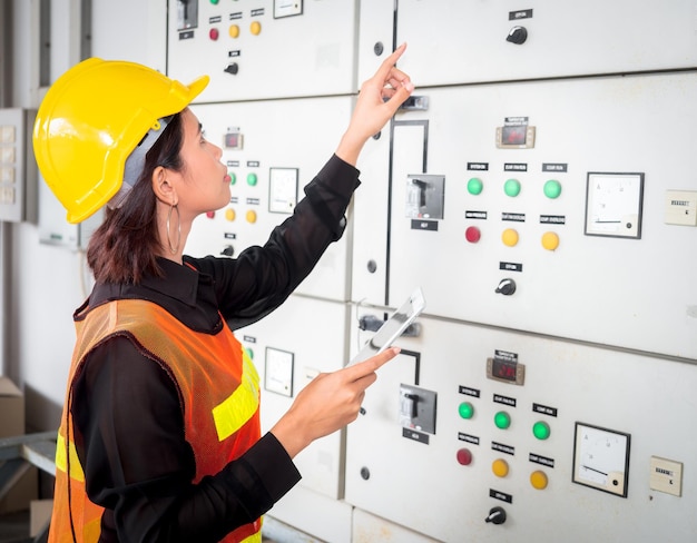 Jovens engenheiras elétricas asiáticas consultam e inspecionam a operação do gabinete de controle elétrico em uma fábrica industrial