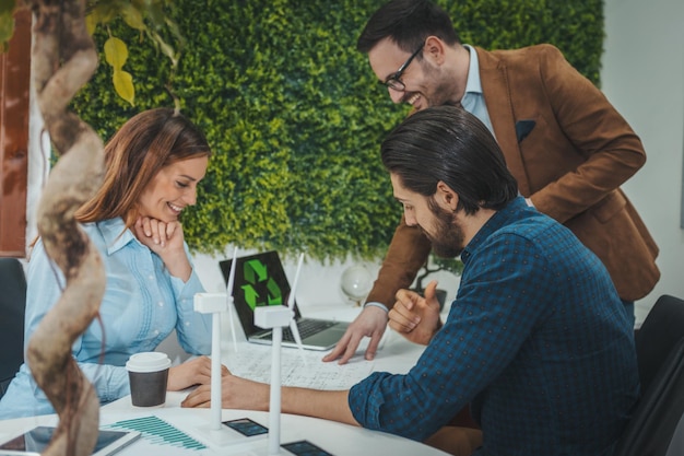 Jovens engenheiros qualificados e inteligentes estão olhando para o projeto de energia alternativa com miniaturas de turbinas de moinho de vento na mesa.