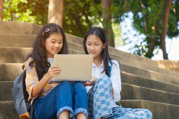 Jovens estudantes asiáticos juntos lendo livro estudo sorrindo com tablet, computador portátil no campus da escola, faculdade em relaxamento de férias de verão