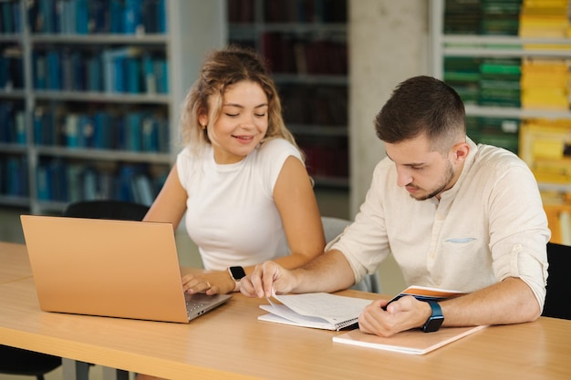 Jovens estudantes felizes de menino e menina se preparando na biblioteca para exame na universidade Duas pessoas estudam Vista traseira dos livros