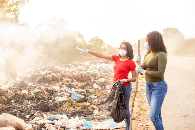 Jovens estudantes negras assistindo a uma área de resíduos enquanto usavam máscaras faciais