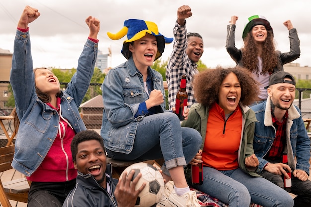 Jovens fãs de futebol intercultural com as mãos levantadas torcendo por seu time favorito durante a transmissão