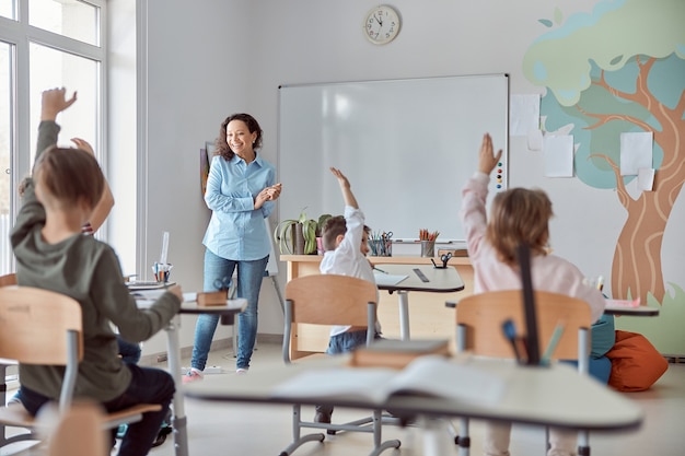 Jovens felizes alunos do ensino fundamental em uma sala de aula moderna estão levantando as mãos para uma lição