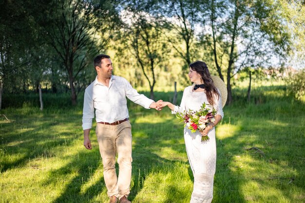 Jovens felizes em trajes de casamento andam no prado e olham uns para os outros