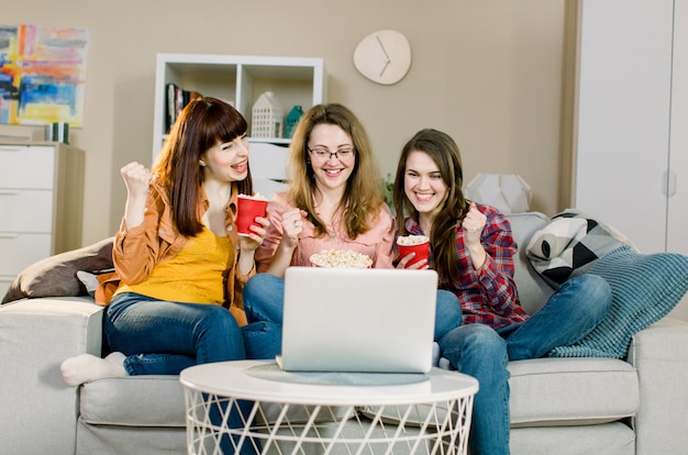 Jovens felizes ou fãs de futebol comendo pipoca enquanto assistia futebol no laptop e comemorando a vitória. Conceito de amizade, esportes e entretenimento.