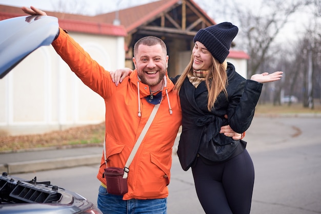 Jovens felizes perto de um carro com o capô aberto.