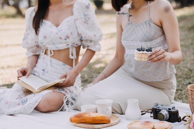 Jovens gêmeas bonitas morenas sentadas na grama com as pernas ligeiramente dobradas nos joelhos e olhando em um livro marrom vestindo casaco casual em clima ensolarado de outono em fundo desfocado