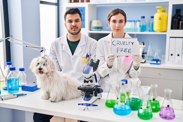 Jovens hispânicos trabalhando no laboratório de cientistas com cachorro relaxado com expressão séria no rosto. olhar simples e natural para a câmera.