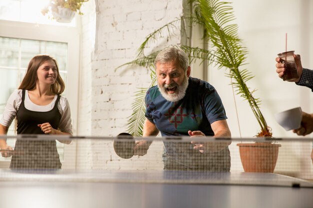 Jovens jogando tênis de mesa no local de trabalho, se divertindo