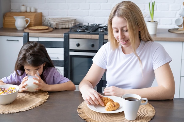 Jovens loiras estão tomando café da manhã com sua filha na cozinha