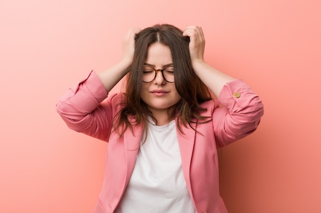 Jovens mais mulher caucasiana de negócios de tamanho tocando os templos e tendo dor de cabeça.