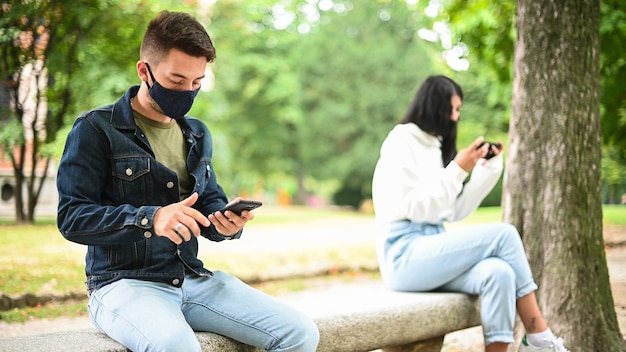 Jovens mantendo o distanciamento social devido ao coronavírus enquanto usam seus telefones ao ar livre em um parque