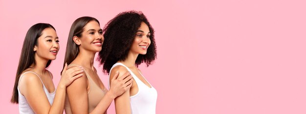 Jovens modelos femininos diversos olhando de lado para o espaço livre posando no panorama de fundo do estúdio rosa