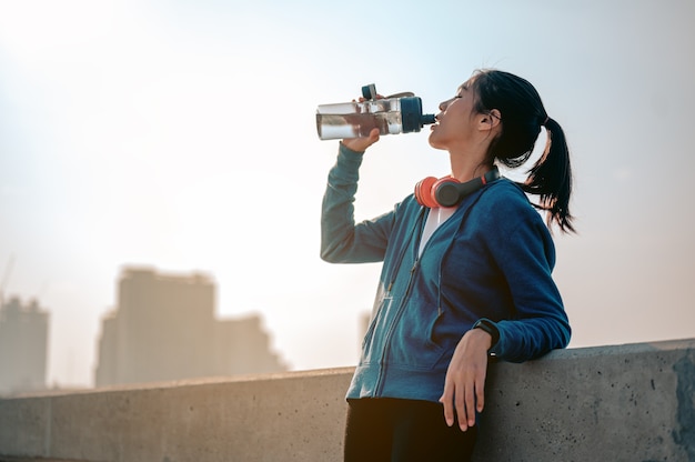 Jovens mulheres asiáticas bebem água e descansam depois de correr para fazer exercícios matinais na cidade