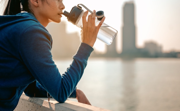 Jovens mulheres asiáticas bebem água e ficam em pé para ver a vista da cidade depois de praticar exercícios matinais de corrida