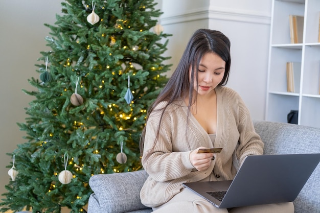 jovens mulheres asiáticas comprando venda online com cartão de crédito usando laptop no sofá em casa, natal
