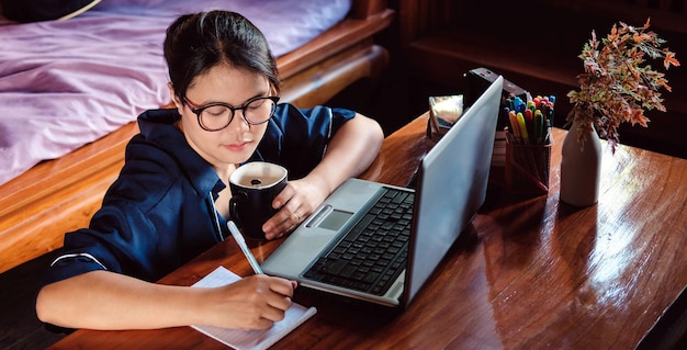 Jovens mulheres asiáticas ou mulheres de negóciosxAWorking Sentem-se em casa com um computador portátil